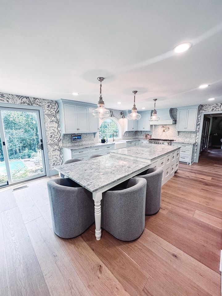Spacious white kitchen with light wood floors, a large island with seating, and a table with four grey chairs.