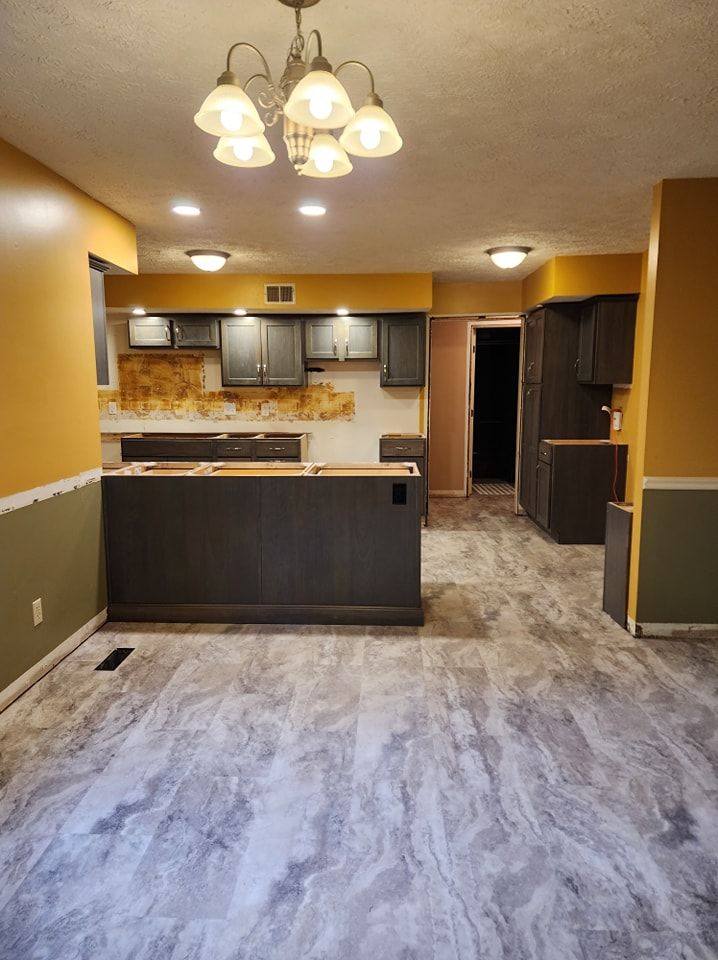 Open-concept kitchen with dark cabinets, a gray island, yellow and green walls, and gray flooring.