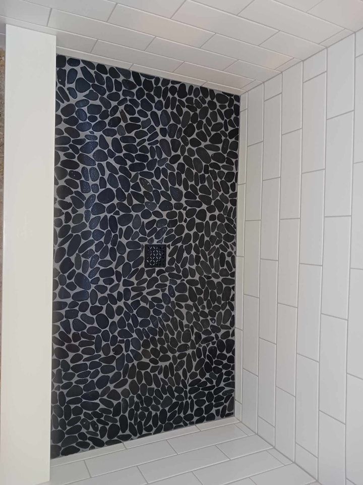 Shower with black pebble tile accent wall and white rectangular wall tiles.