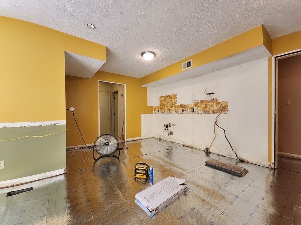 Basement under renovation with exposed wall, flooring, tools, and mustard yellow and green walls.