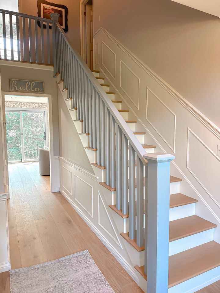 Staircase with light blue railing and white paneling, leading to a second floor. Light wood floors and tan walls.