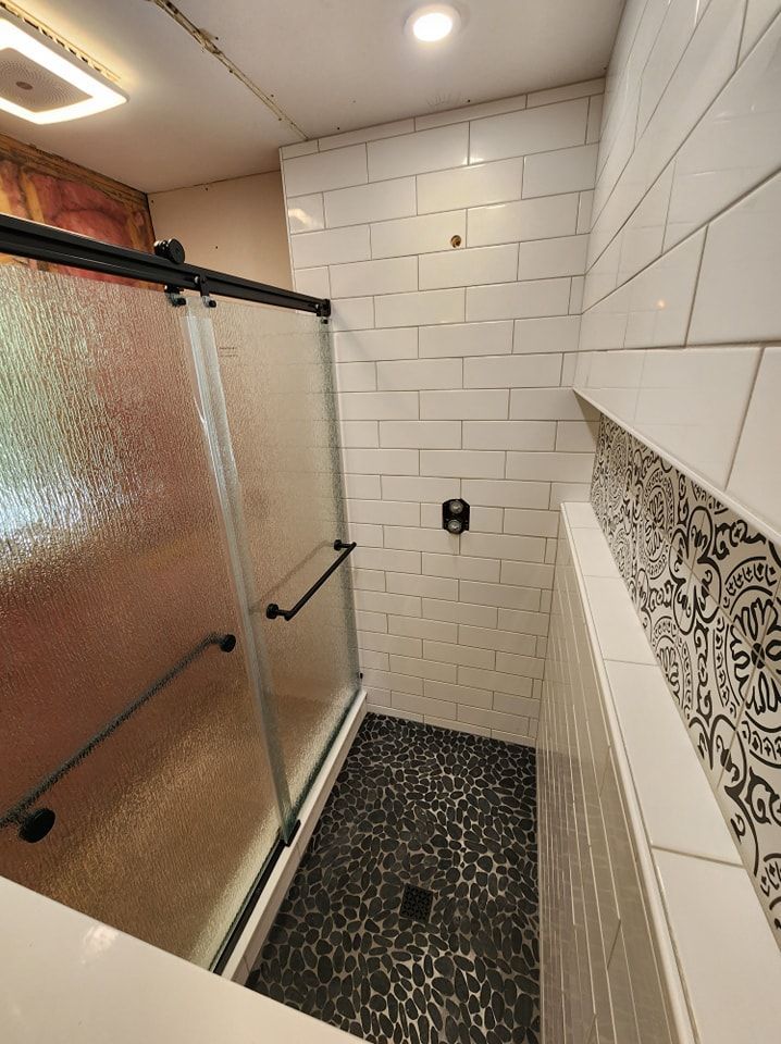 Shower with black pebble floor, white subway tile walls, and glass sliding door.