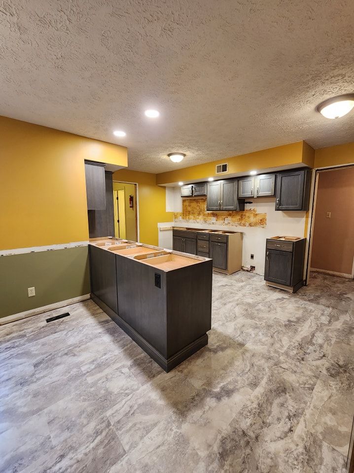 Newly renovated kitchen with gray cabinets, island, and flooring; yellow and green walls.