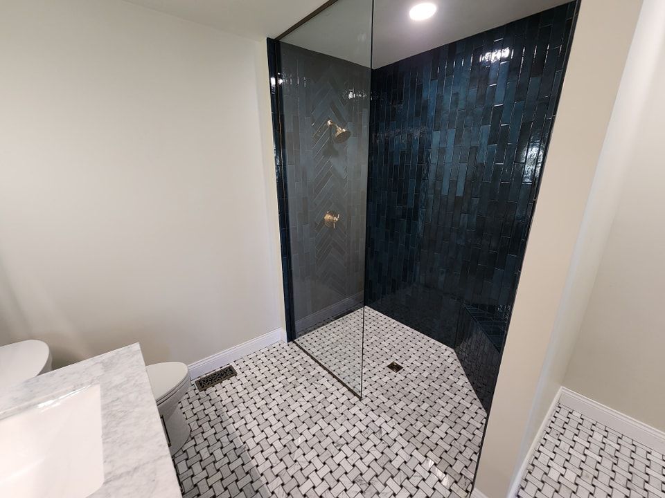 A modern bathroom with a blue-tiled shower, glass door, and mosaic floor.