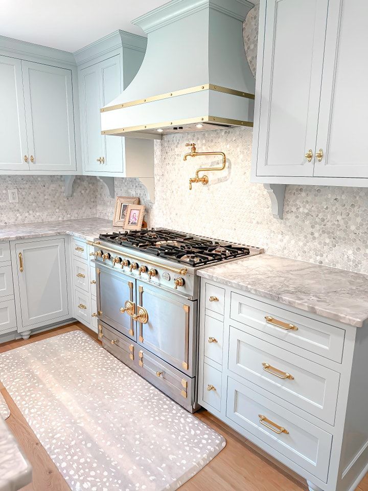 Light blue kitchen with stainless steel stove, gold hardware, and patterned rug.