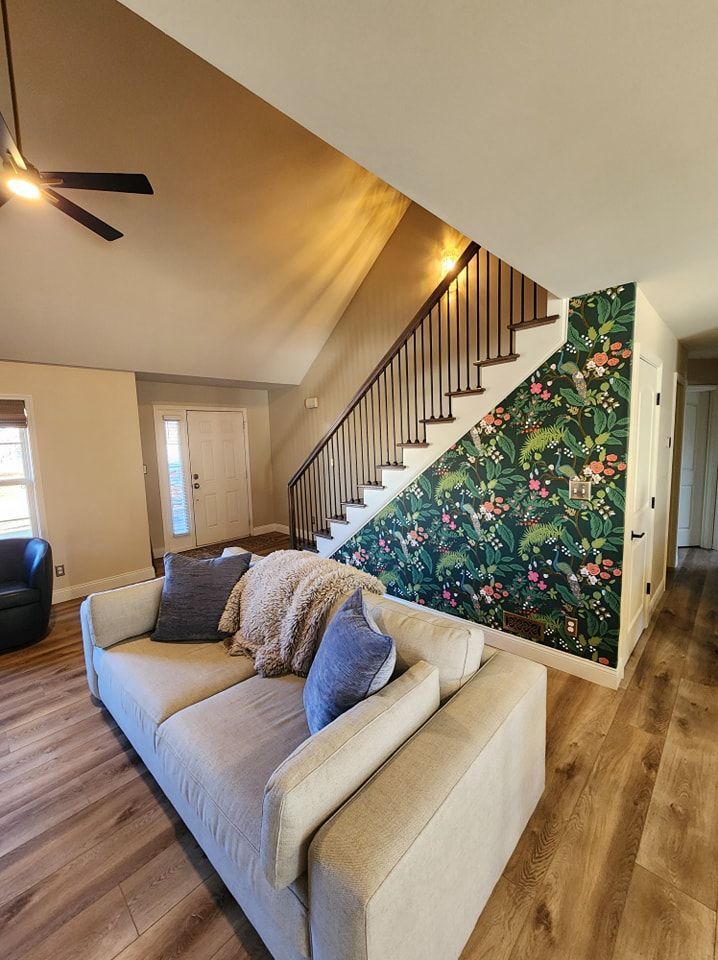 Living room with floral accent wall, staircase, beige couch, and wood flooring.