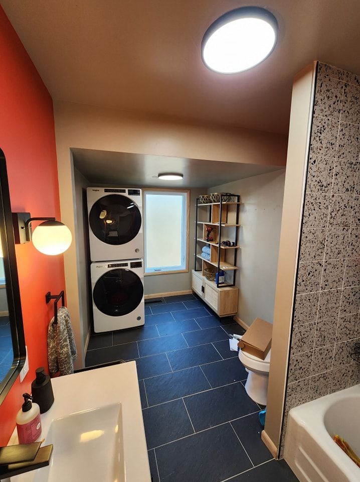 Bathroom with stacked washer/dryer, sink, toilet, shelves, and dark blue tile floor.