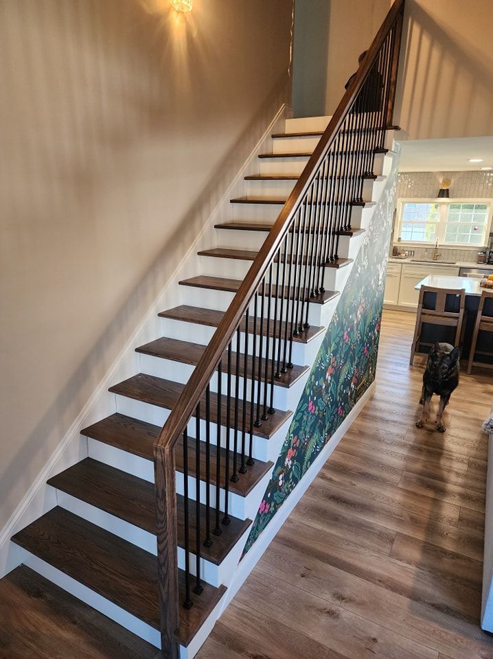 Staircase with brown treads, white risers, dark metal spindles, and a floral wallpaper accent. Wooden floors.