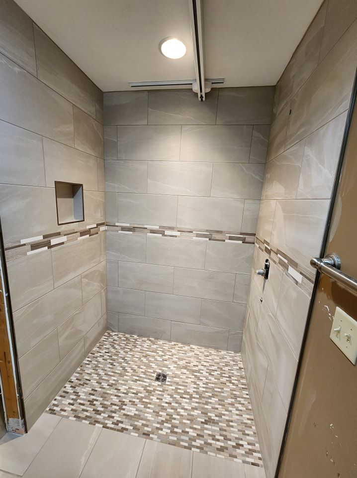 Newly tiled shower with gray walls and a mosaic floor.  A niche and a dark fixture are visible.