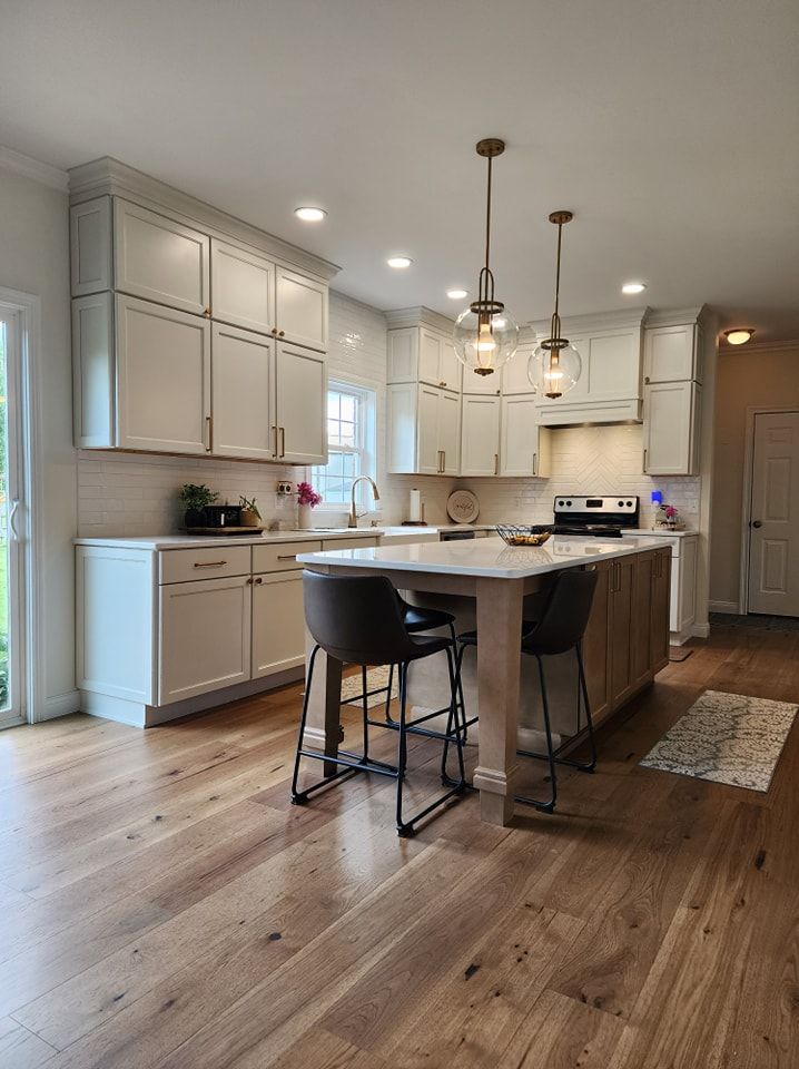 Modern kitchen with light cabinets, wood floor, island with stools, pendant lights.