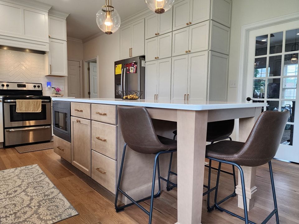 Kitchen with island and barstools, light cabinets, stainless steel appliances, and wooden floors.