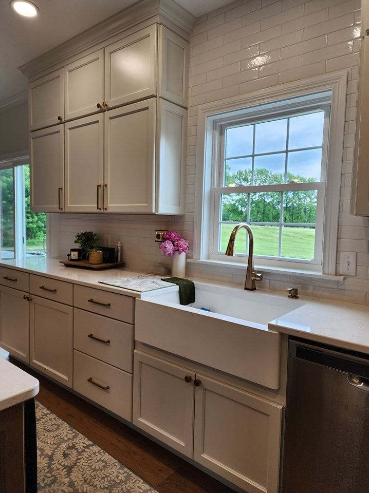Cream-colored kitchen cabinets and farmhouse sink, window overlooking a green field.