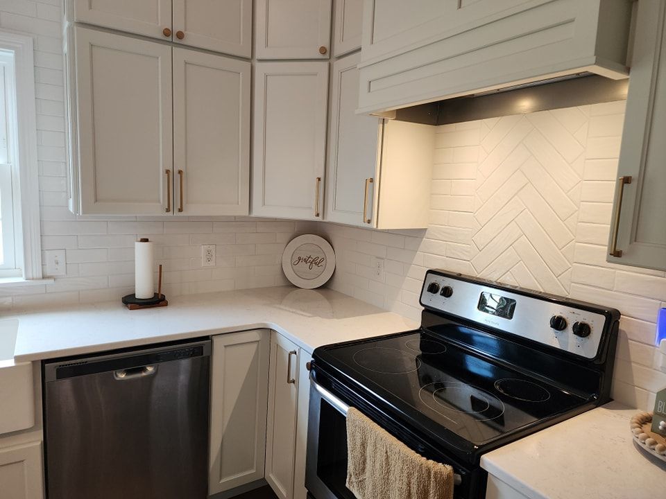 White kitchen with cabinets, stainless steel appliances, and herringbone backsplash.