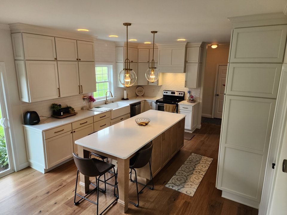 Modern kitchen with white cabinets, island with stools, hardwood floors, and overhead lights.
