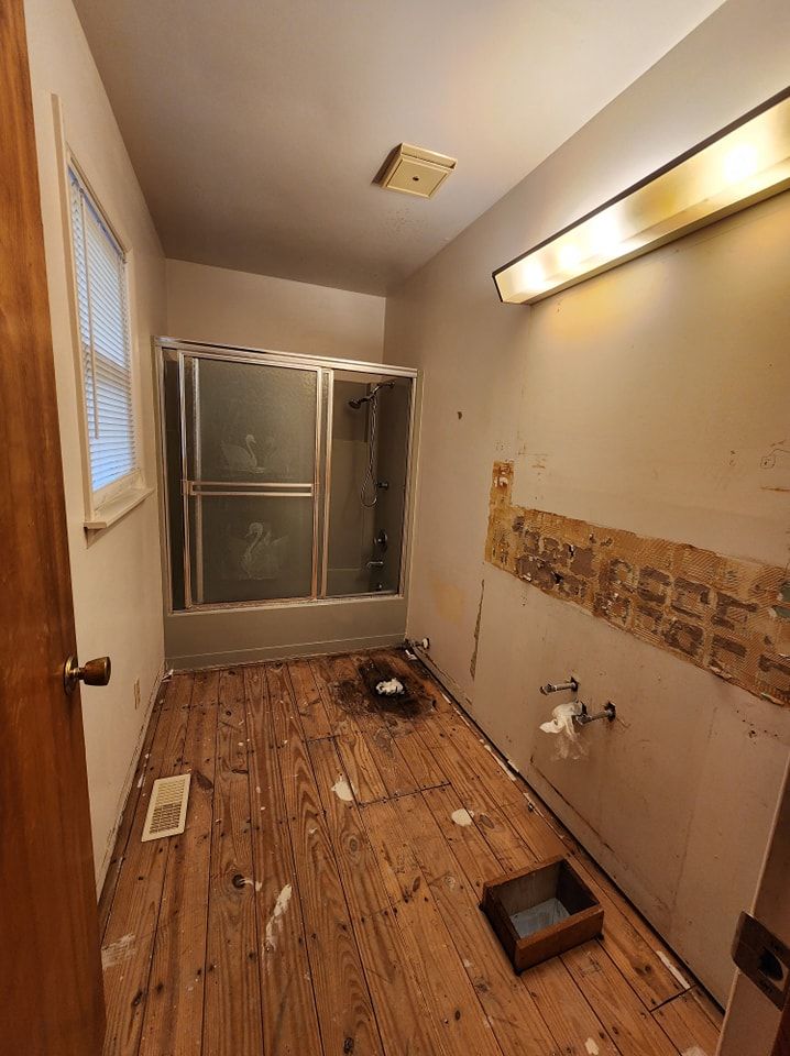 Bathroom with wood floor, shower stall, and exposed wall. Door is open.
