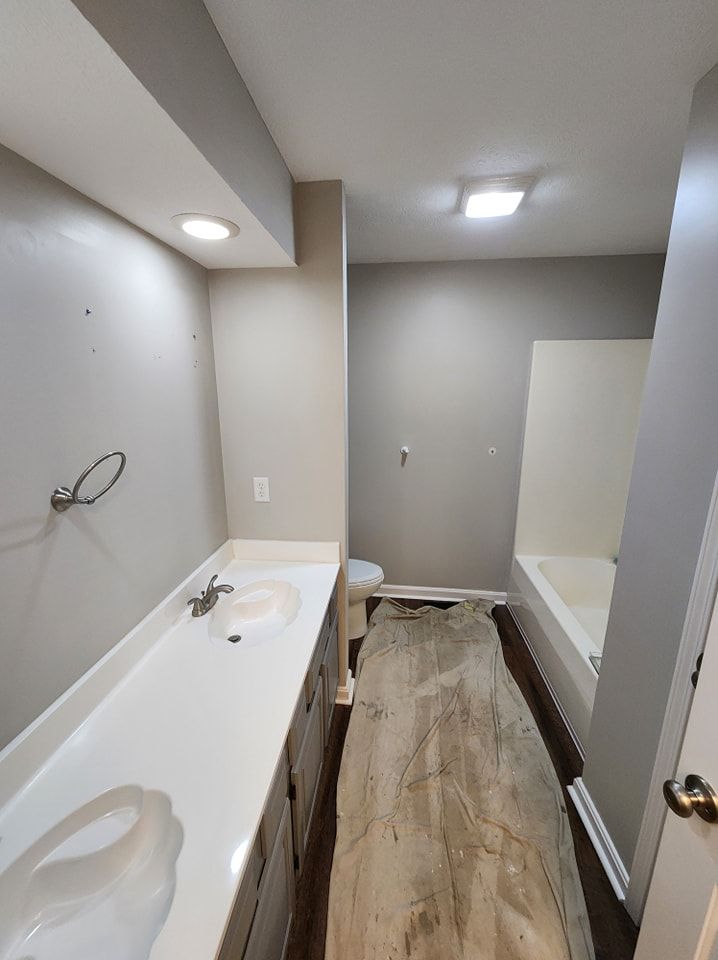 Bathroom renovation in progress. Gray walls, long countertop, partial flooring, and bathtub visible.