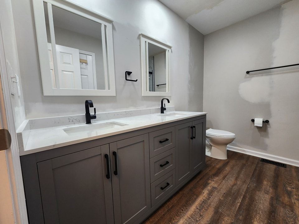 Gray double vanity bathroom with white countertop, black fixtures, and brown wood-look floor.