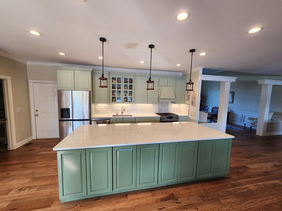 Green kitchen with island and pendant lights; hardwood floors.