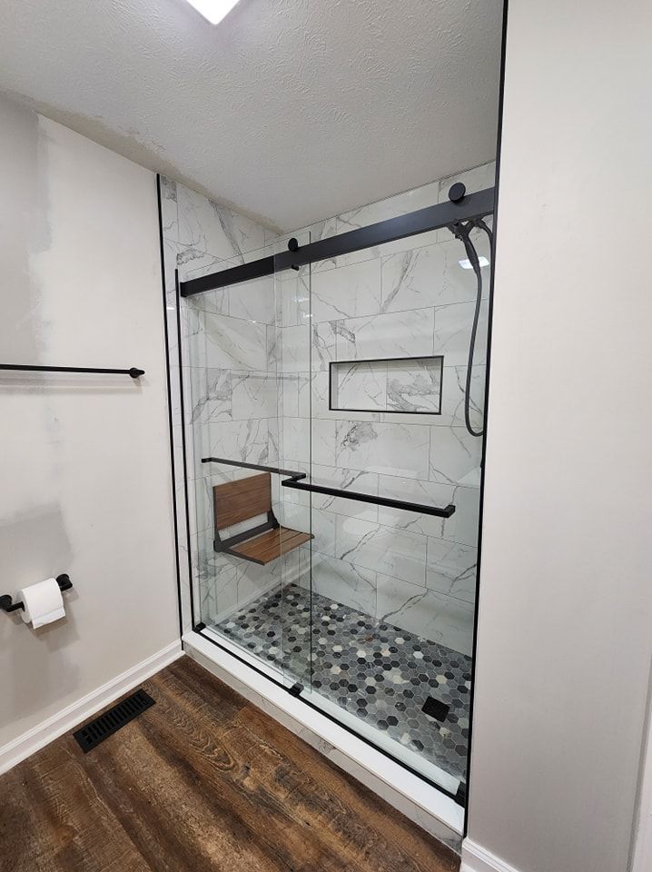 Modern bathroom with glass shower enclosure, black trim, marble tile, and a built-in seat.