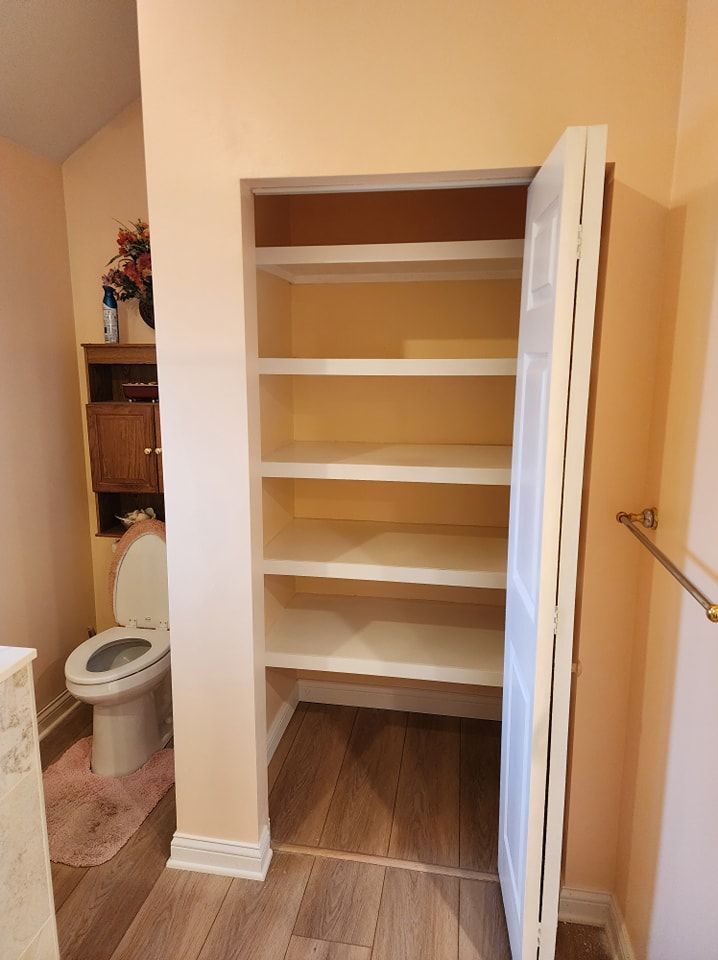 Bathroom closet with open white door, shelves, and toilet.