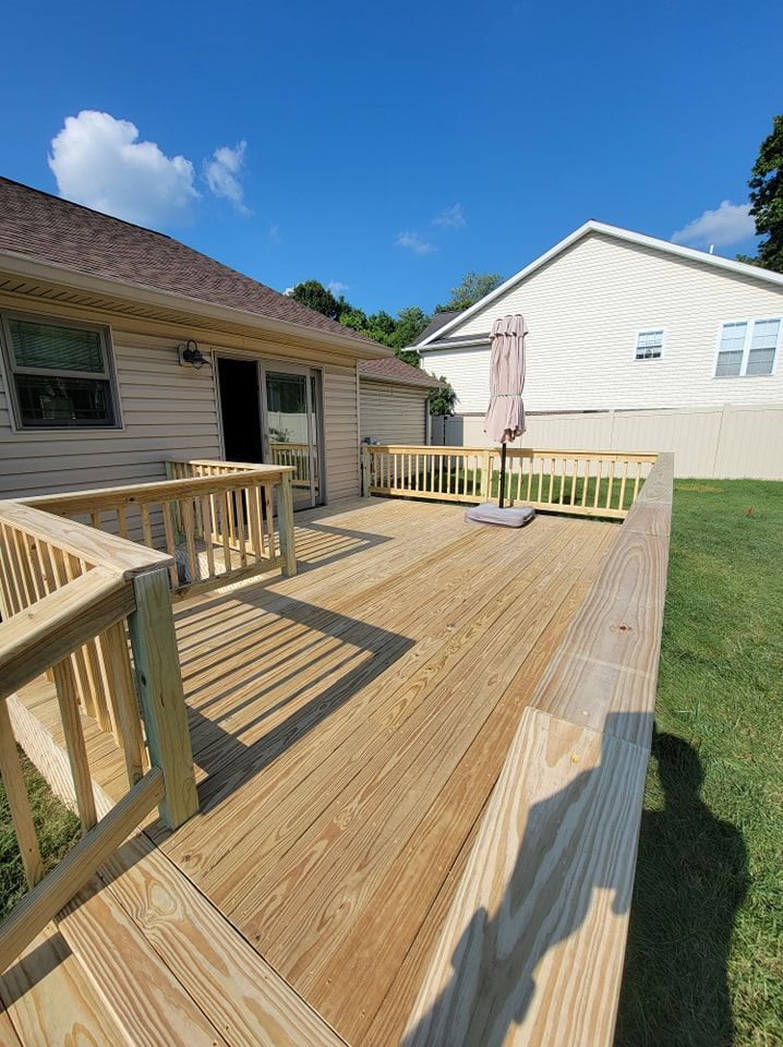 Wooden deck with railings, attached to a house with a door, umbrella, and clear blue sky.