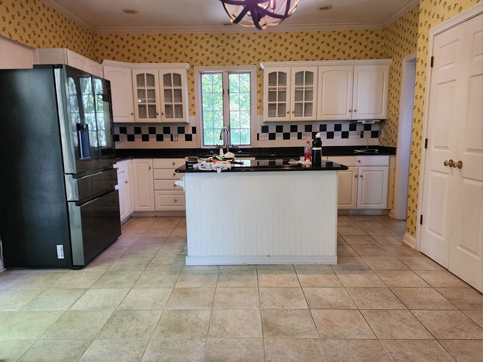 Kitchen with white cabinets, black countertops, and a black refrigerator; yellow patterned wallpaper.