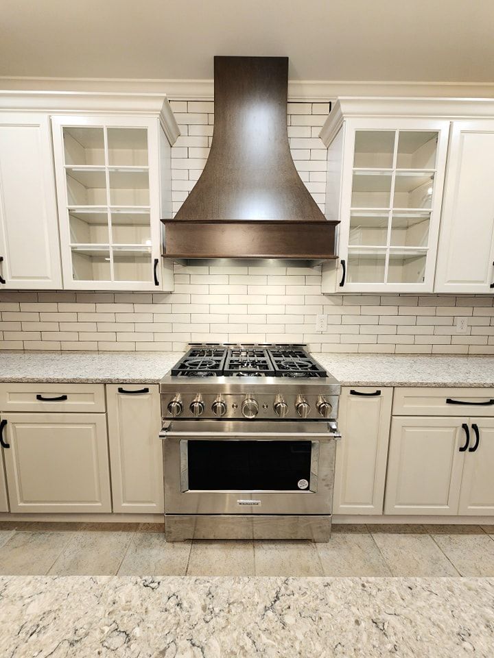 Stainless steel range centered in a kitchen with white cabinets, a dark wood range hood, and subway tile backsplash.
