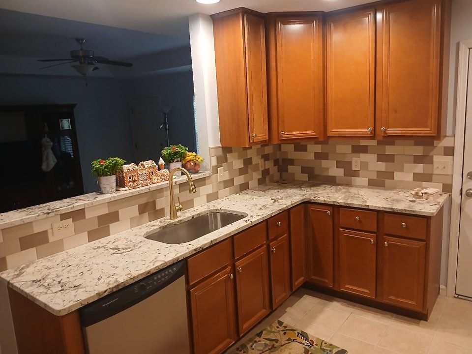 Kitchen with light granite countertops, brown cabinets, and a backsplash with mosaic tiles.