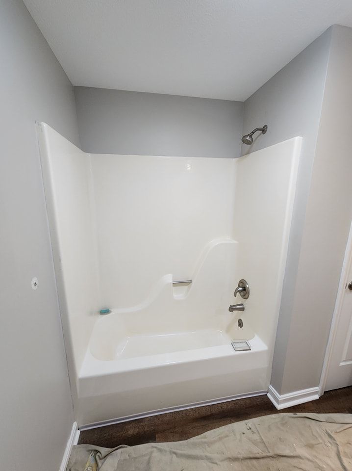 White bathtub and shower surround in a bathroom with gray walls and wood-look flooring.