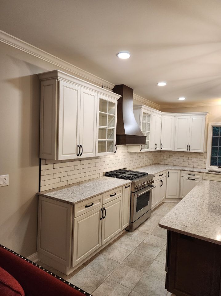 White kitchen with stainless steel appliances, dark hood, granite countertops, and tile backsplash.