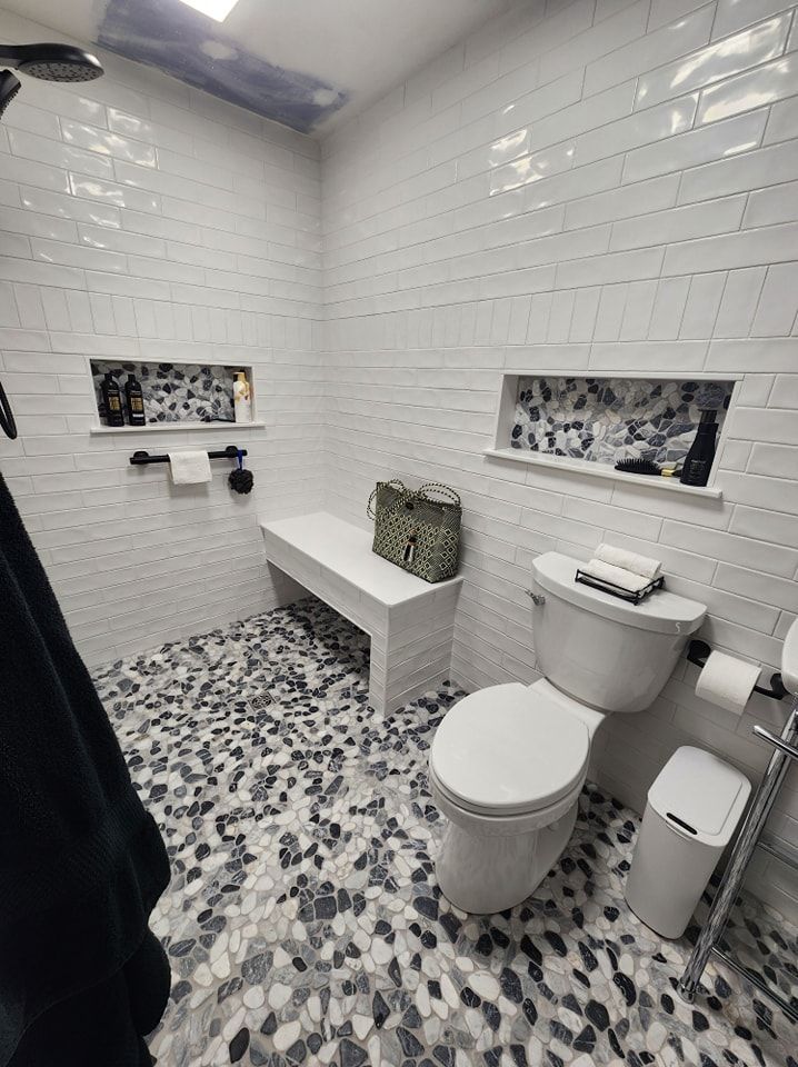 Bathroom with white tile walls, pebble floor, built-in bench, toilet, and two recessed shelves.