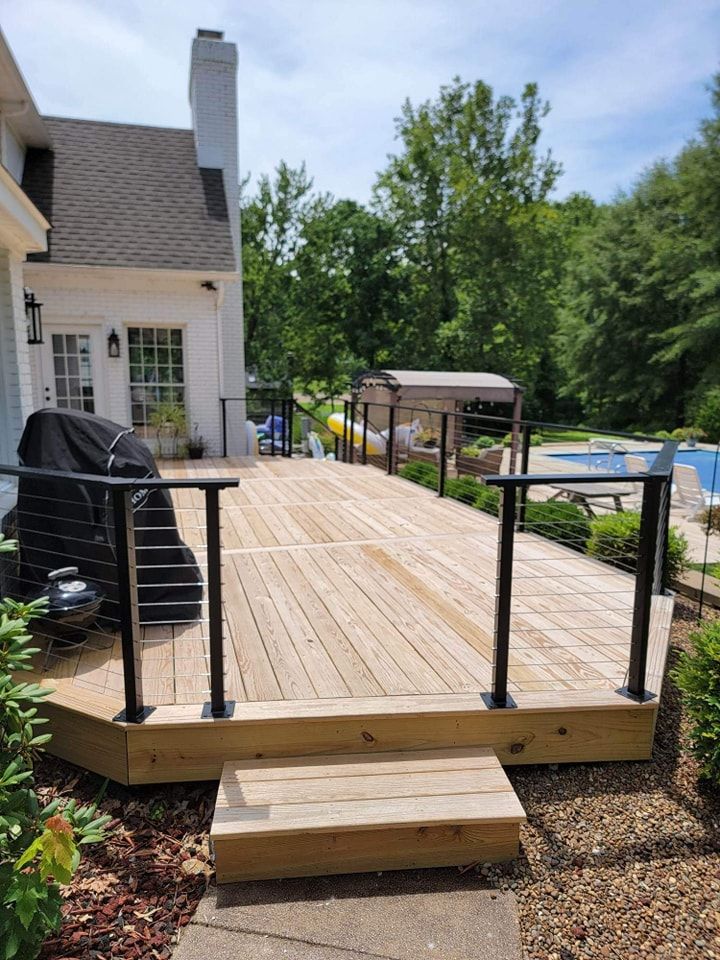 Wooden deck with black railings and steps, near a house and pool.