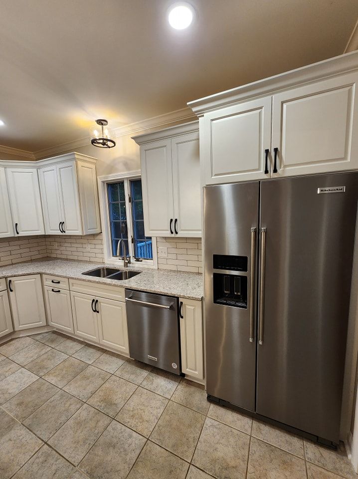 White kitchen cabinets with stainless steel appliances, brick backsplash, and tiled floor.