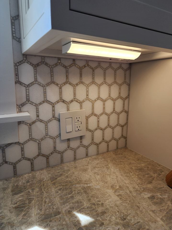 Kitchen backsplash with honeycomb tile, light fixture above, and outlet.
