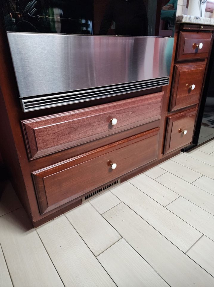 A kitchen island with a stainless steel appliance, drawers, and a dark wooden cabinet, sitting on a light-colored tiled floor.