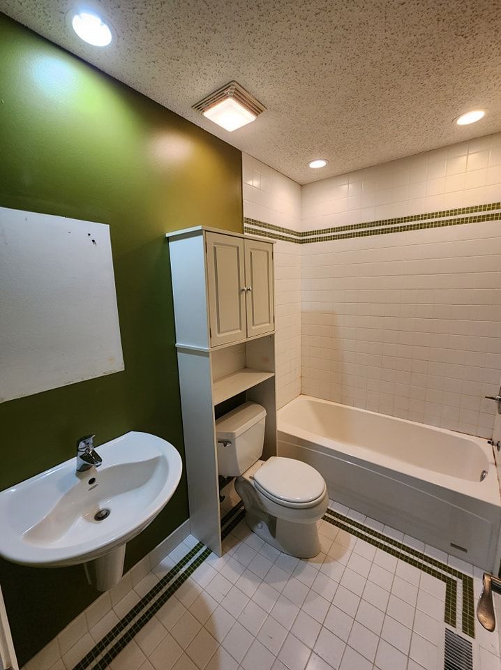 Bathroom with green and white tiled floor, green wall, white pedestal sink, toilet, and cabinet.