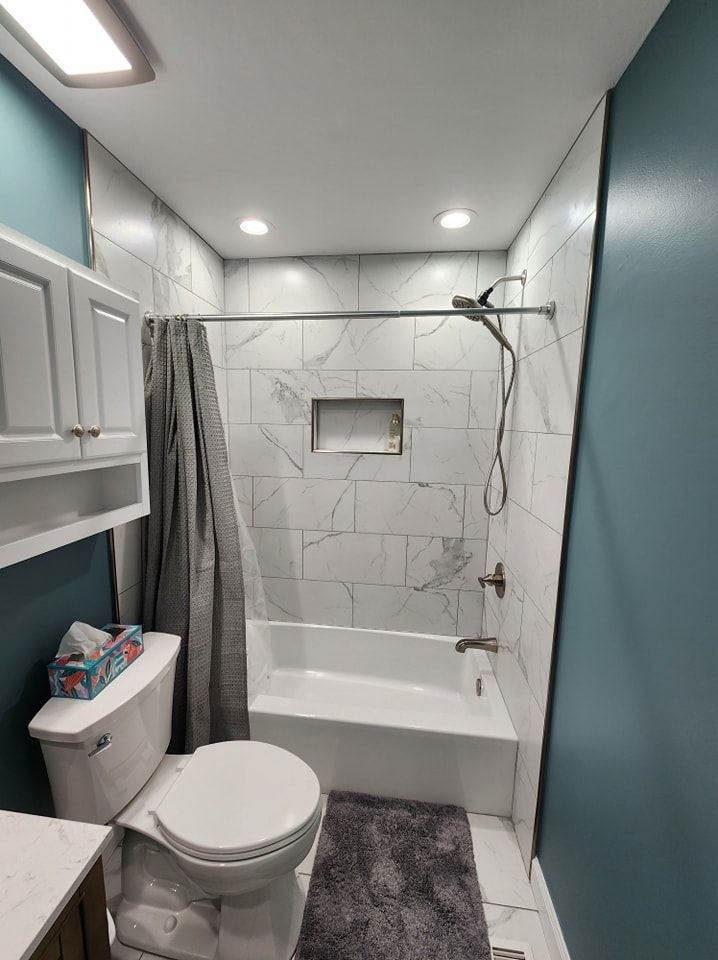 Bathroom with white marble tile shower, blue walls, toilet, and gray rug.