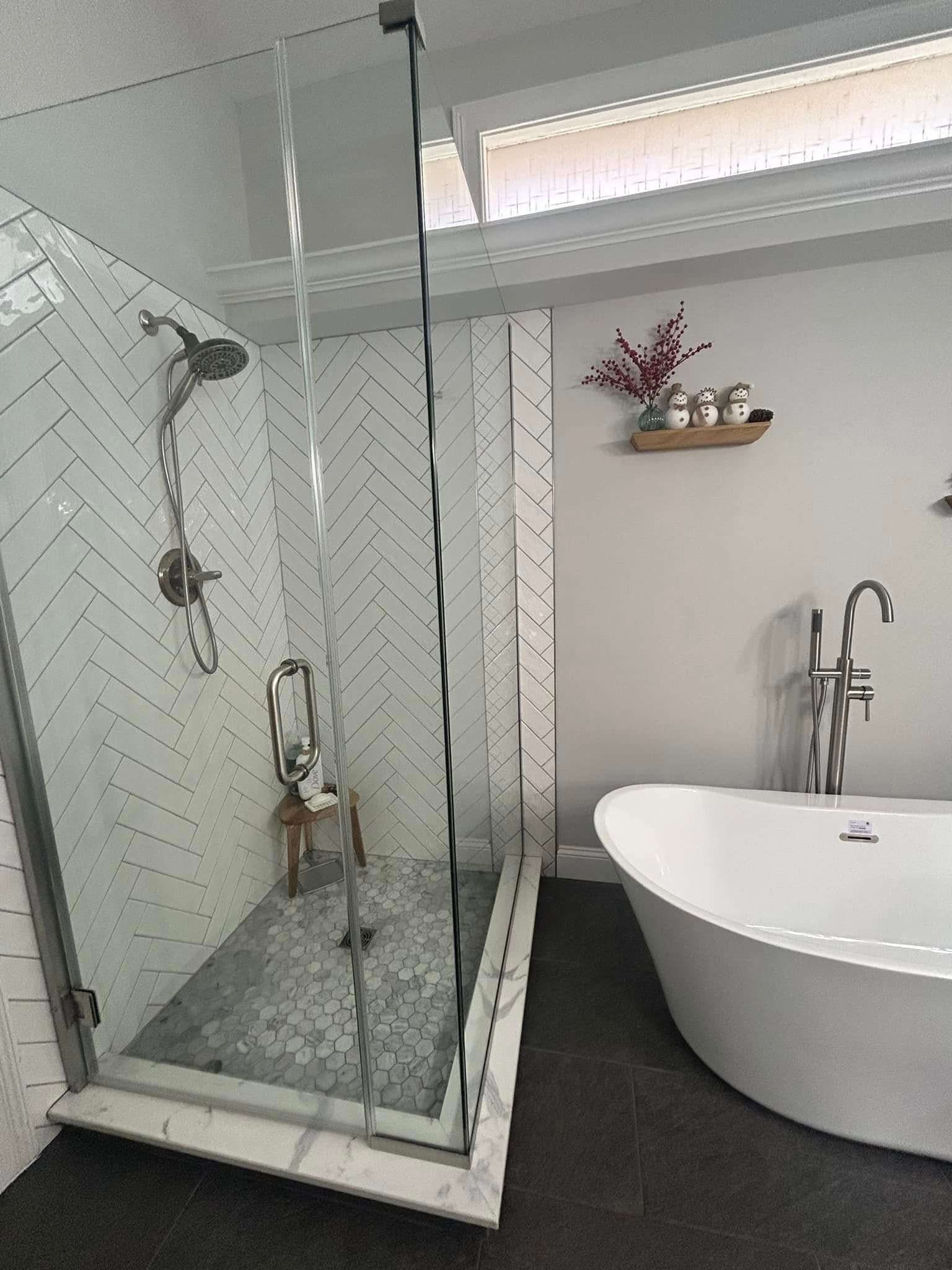 Modern bathroom with a glass-enclosed shower, freestanding tub, and a small decorative shelf. White and grey.