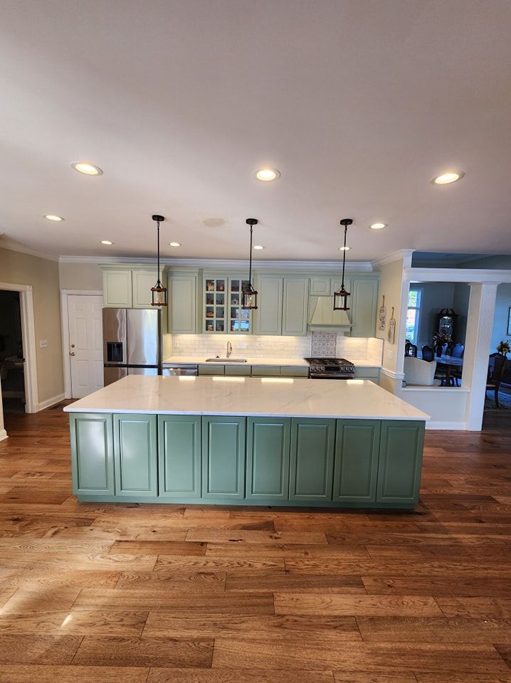 Green and white kitchen with a large island and hardwood floors.