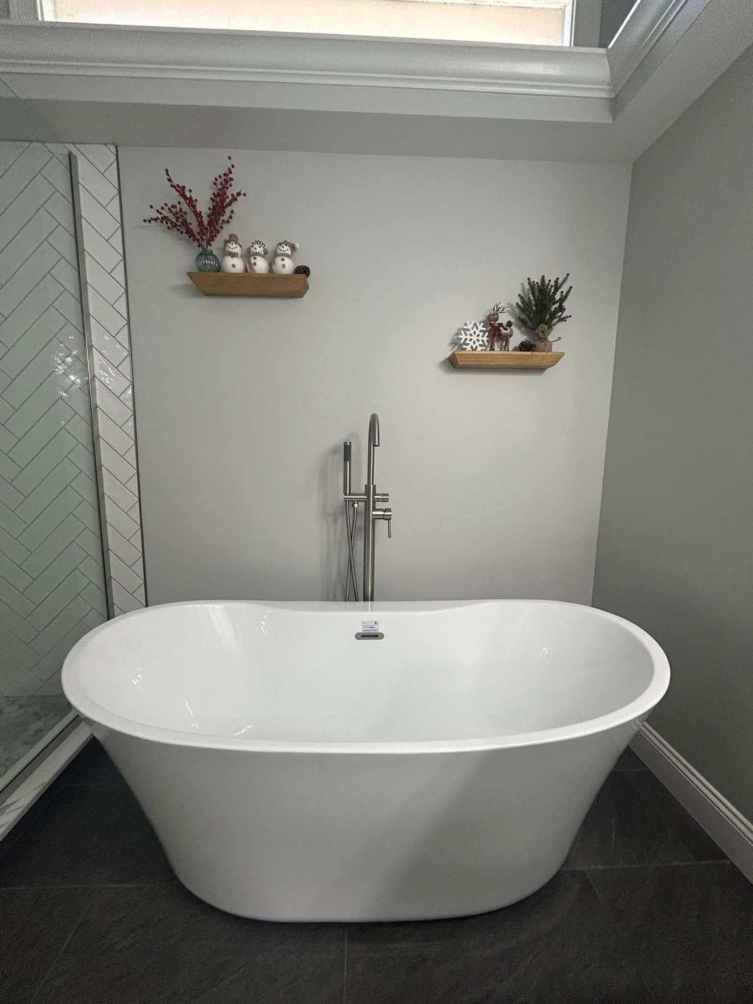 Modern bathroom with white freestanding tub, chrome faucet, and decorative shelves on a gray wall.