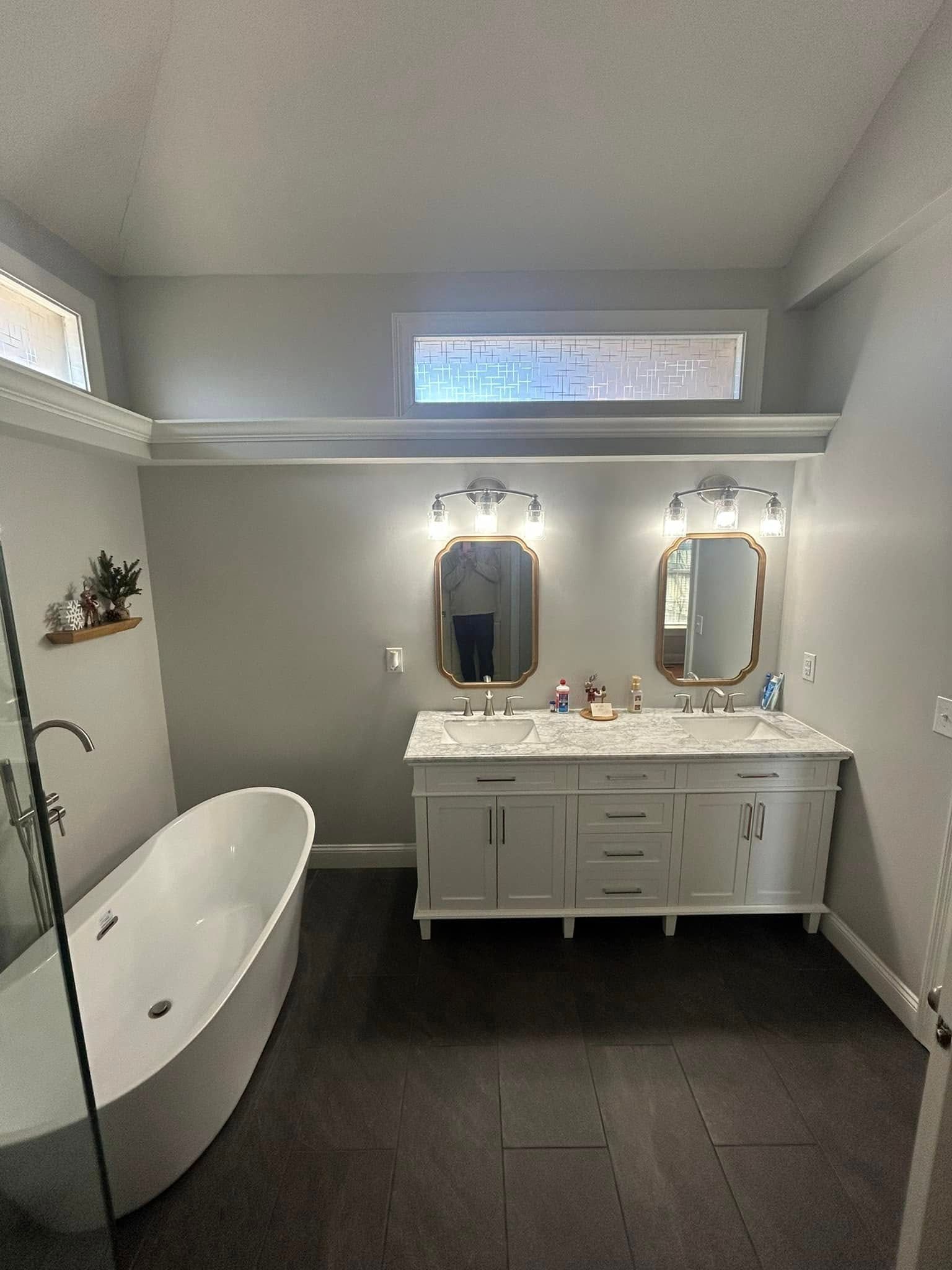 Bathroom with a white soaking tub, double vanity with mirrors, and gray walls and dark flooring.