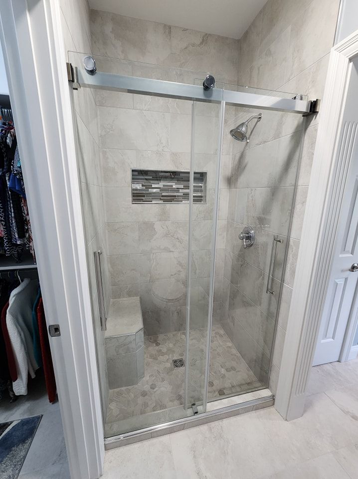 Modern shower with sliding glass door, tiled walls, built-in bench, and chrome fixtures.