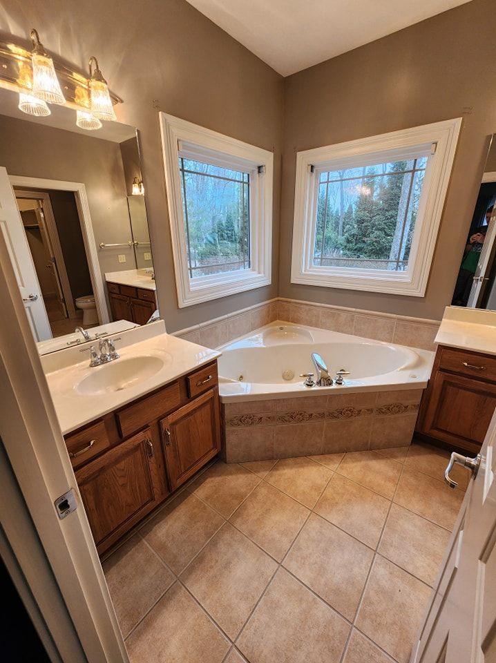 Bathroom with a corner bathtub, windows, beige tile floor, and oak cabinets.