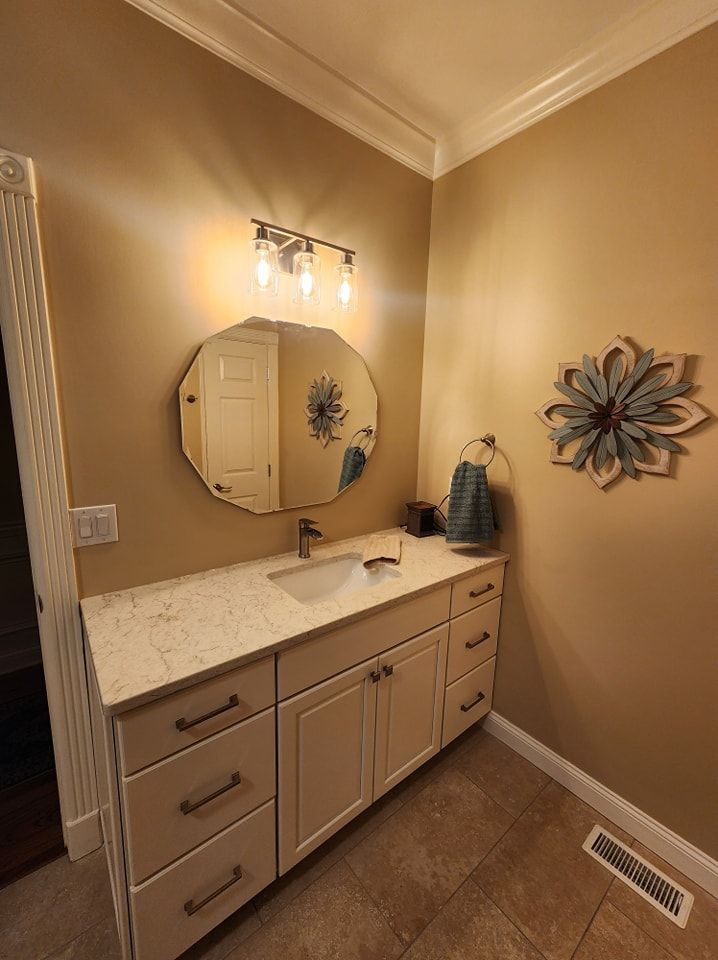 Bathroom vanity with oval mirror, cream cabinets, quartz countertop, and tan walls.