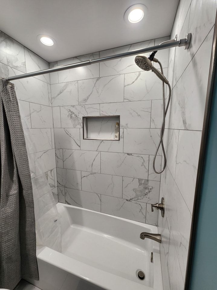 Modern bathroom with white marble-look tiles, a white bathtub, and silver shower fixtures.