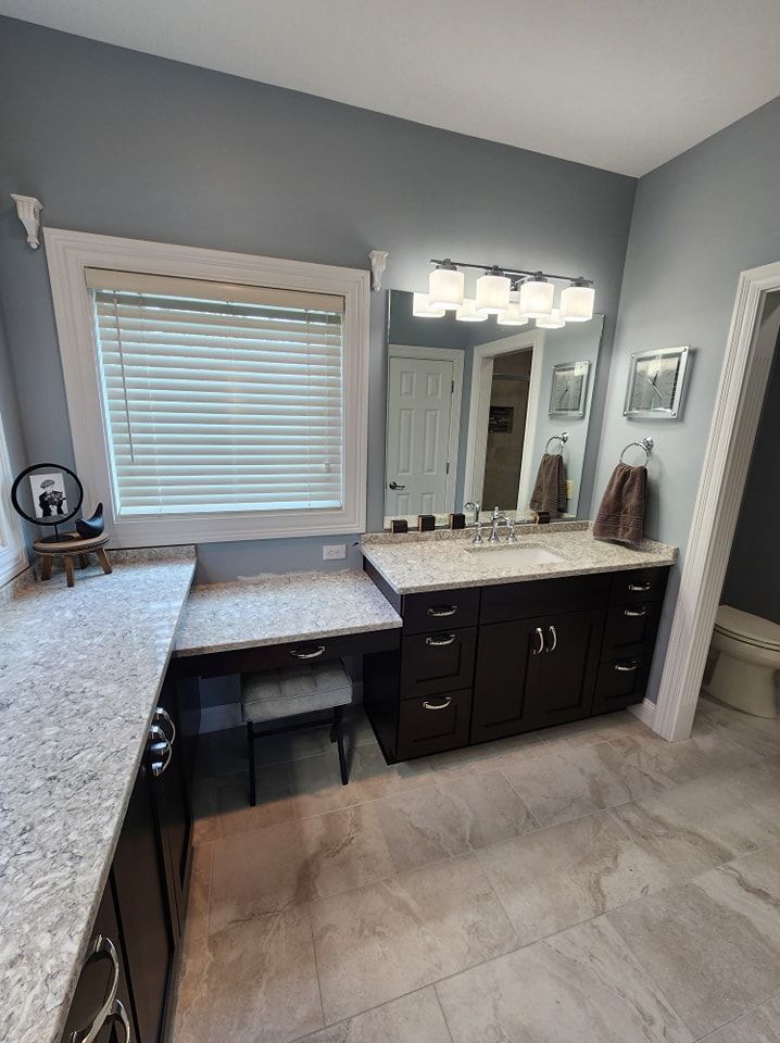Bathroom with dark brown vanity, gray walls, granite countertops, and a window with blinds.