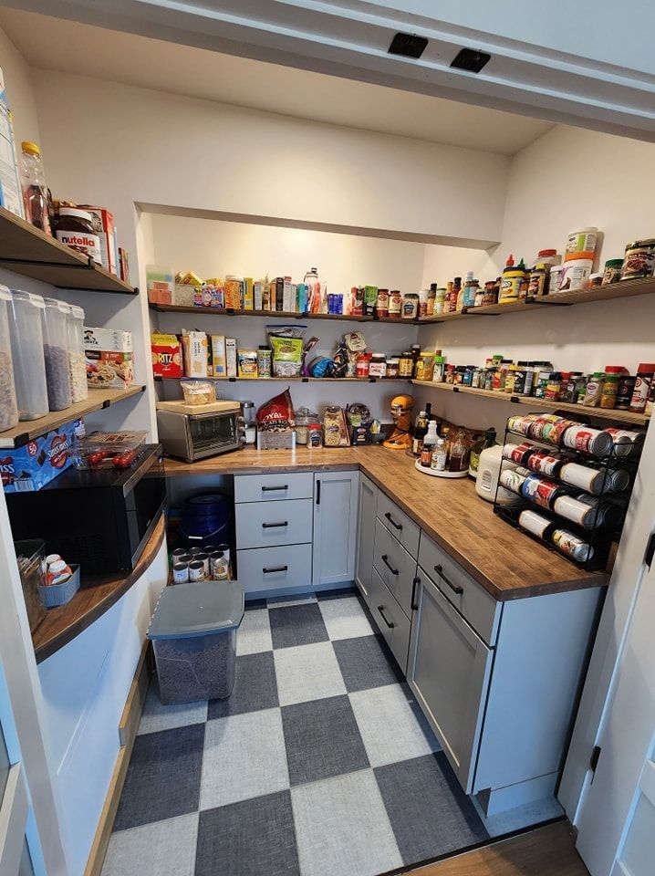 Pantry with gray cabinets, wood counters, checkerboard floor, and shelves stocked with food items.