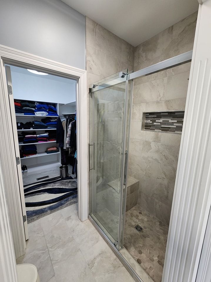 Bathroom with shower and walk-in closet. Gray tile, sliding glass door, and white trim.
