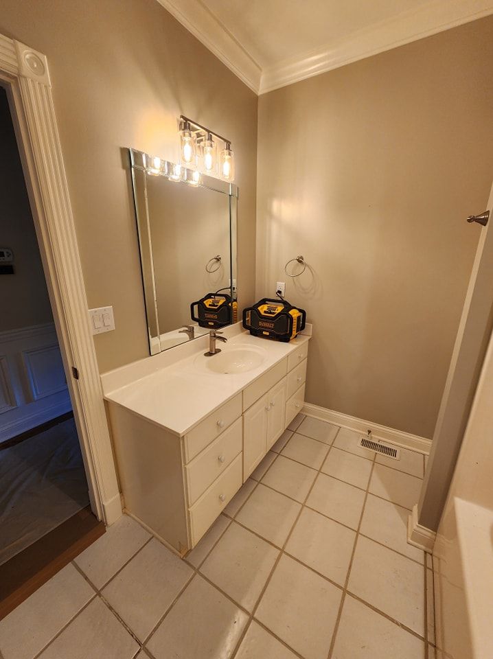 Bathroom with white vanity, mirror, and a light fixture over the sink. Light-colored walls and tiled floor.