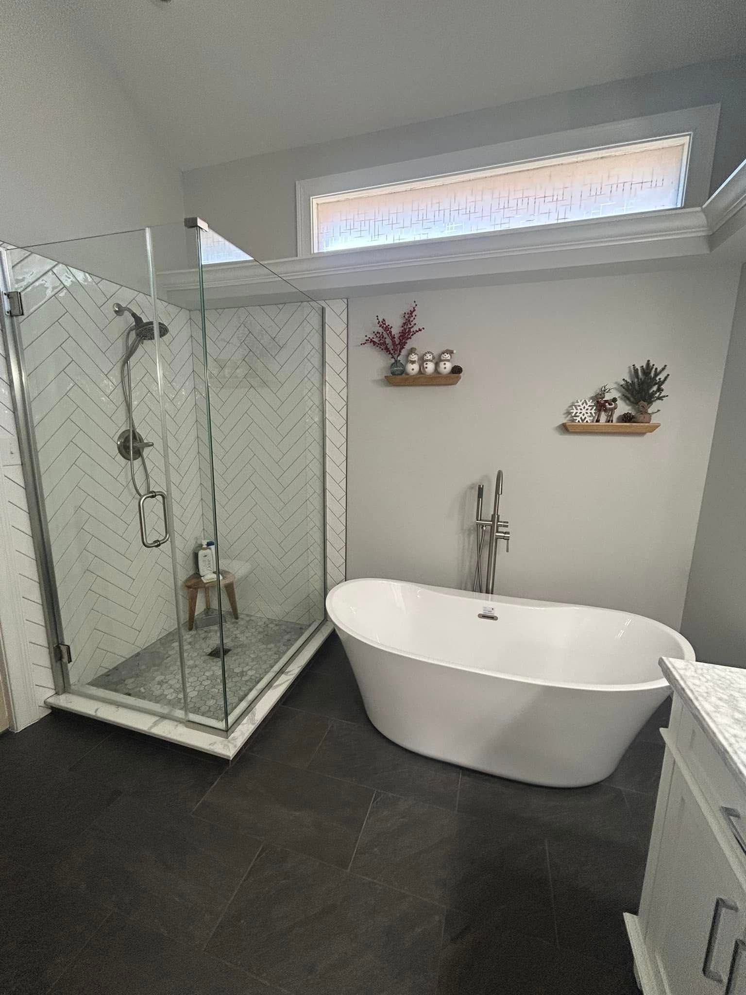 Modern bathroom with a glass-enclosed shower, freestanding tub, and small shelves with decor.